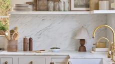 A kitchen with warm neutral cabinets and a marble countertop, backsplash, and shelf decorated with curated decor from Shoppe Amber Interiors 
