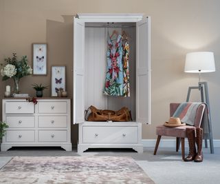 white freestanding wardrobe with door open showing dress hanging and large bag on shelf underneath