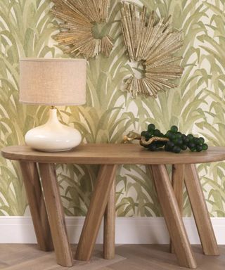 An entryway with green leafy wallpaper and a wooden table with a white lamp on