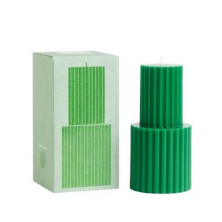 A bright green two-tiered ridged pillar candle next to a sage green box with an illustration on it on the front