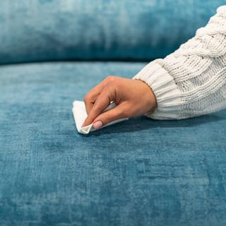 Woman cleaning a blue sofa with white cloth