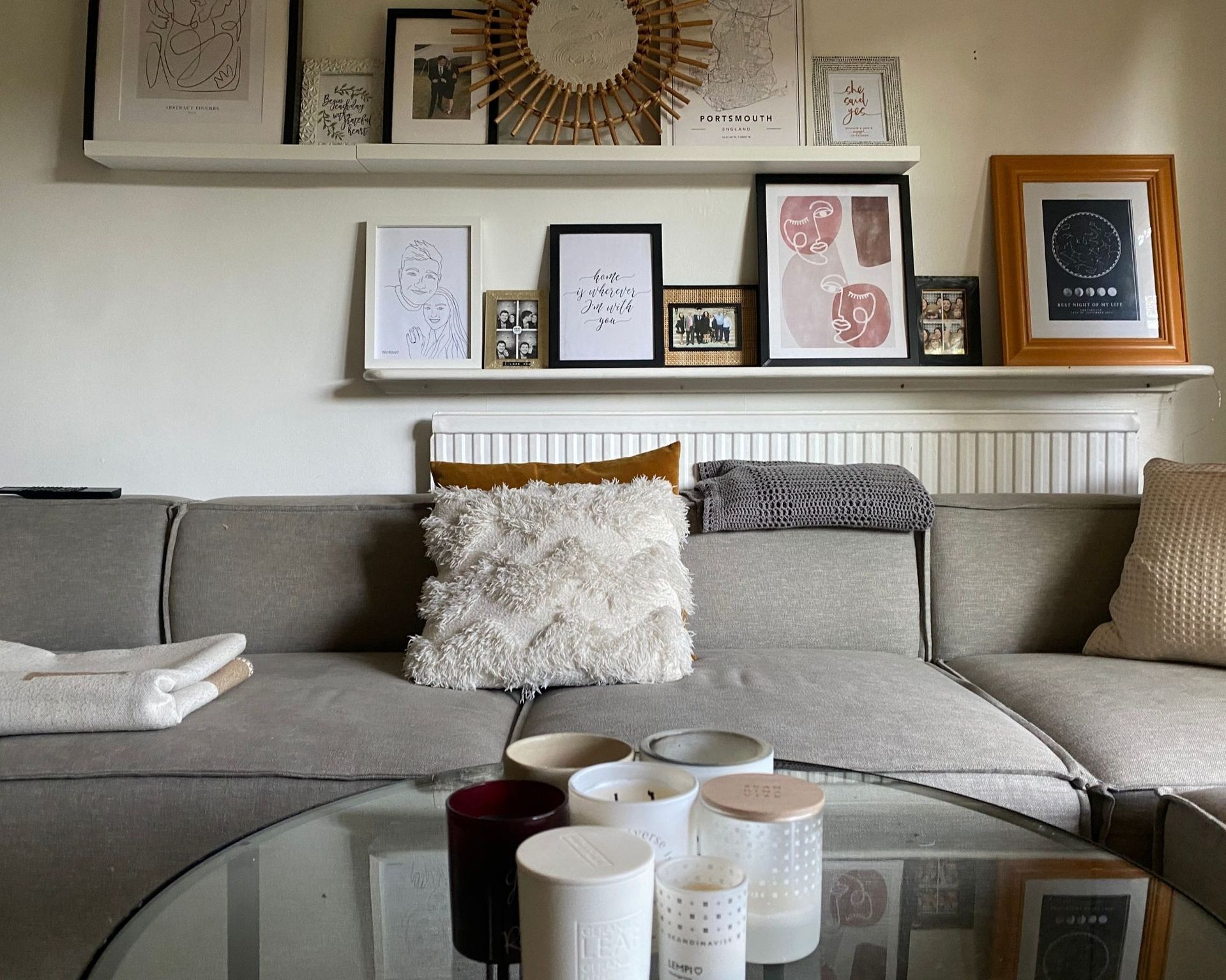 Range of candles from this guide on glass coffee table in front of grey sofa with gallery wall,