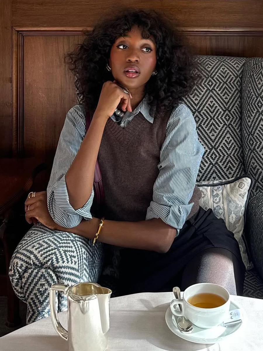 Emmanuelle Koffi drinks tea while wearing a button-down shirt and vest.