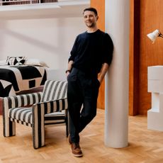 Interior Design Masters series 6 winner, John Cooper leaning against a pillar, surrounded by pieces from his John Lewis collection
