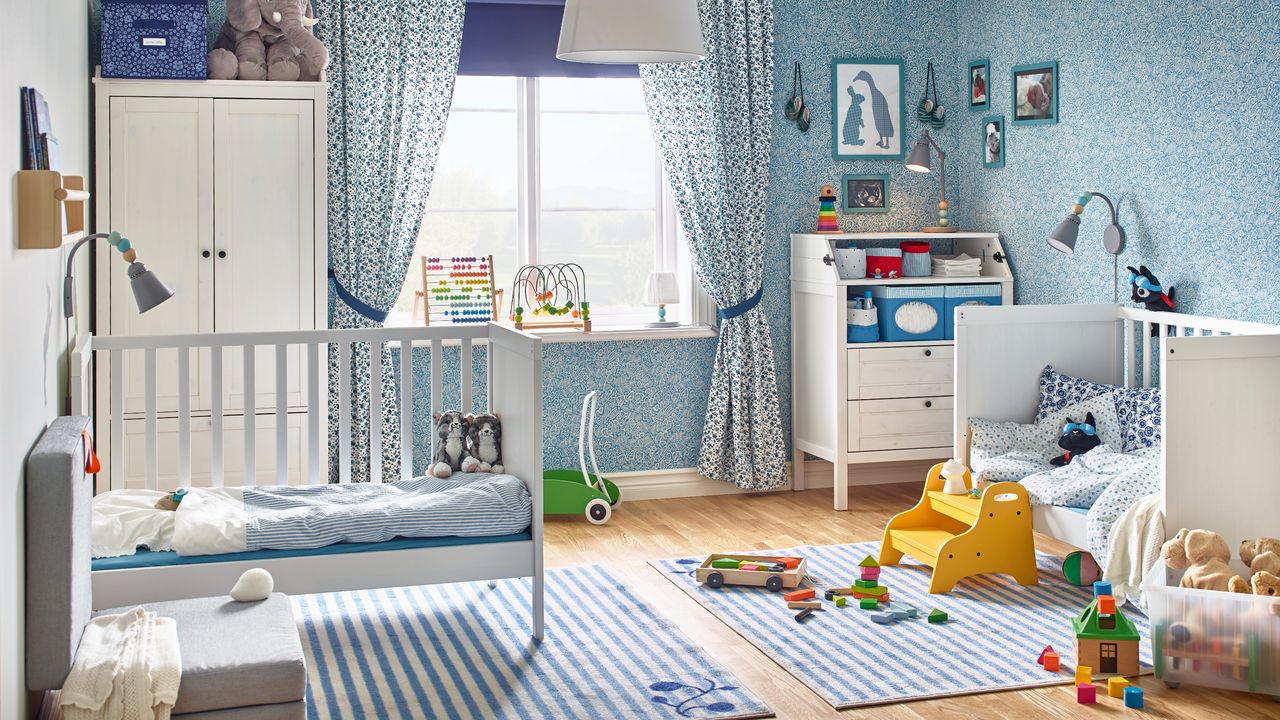 Twin nursery ideas: two white childrens beds with blue striped bedding, stripey rugs on wood floor in front of blue patterned wall and curtains