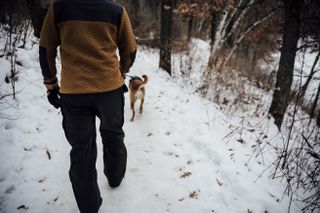 A man walks on a snow covered trail with a dog