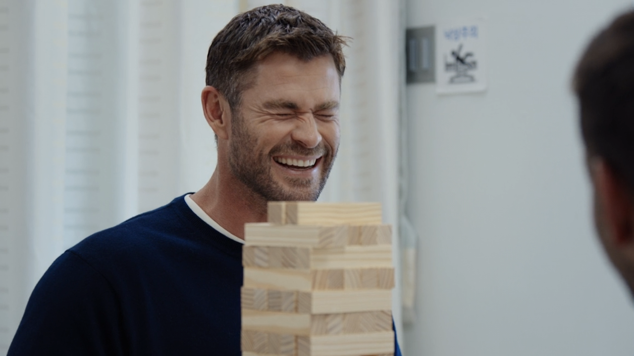 Chris Hemsworth smiling and squinting in pain while being shocked during a Jenga game in Limitless Live Better Now