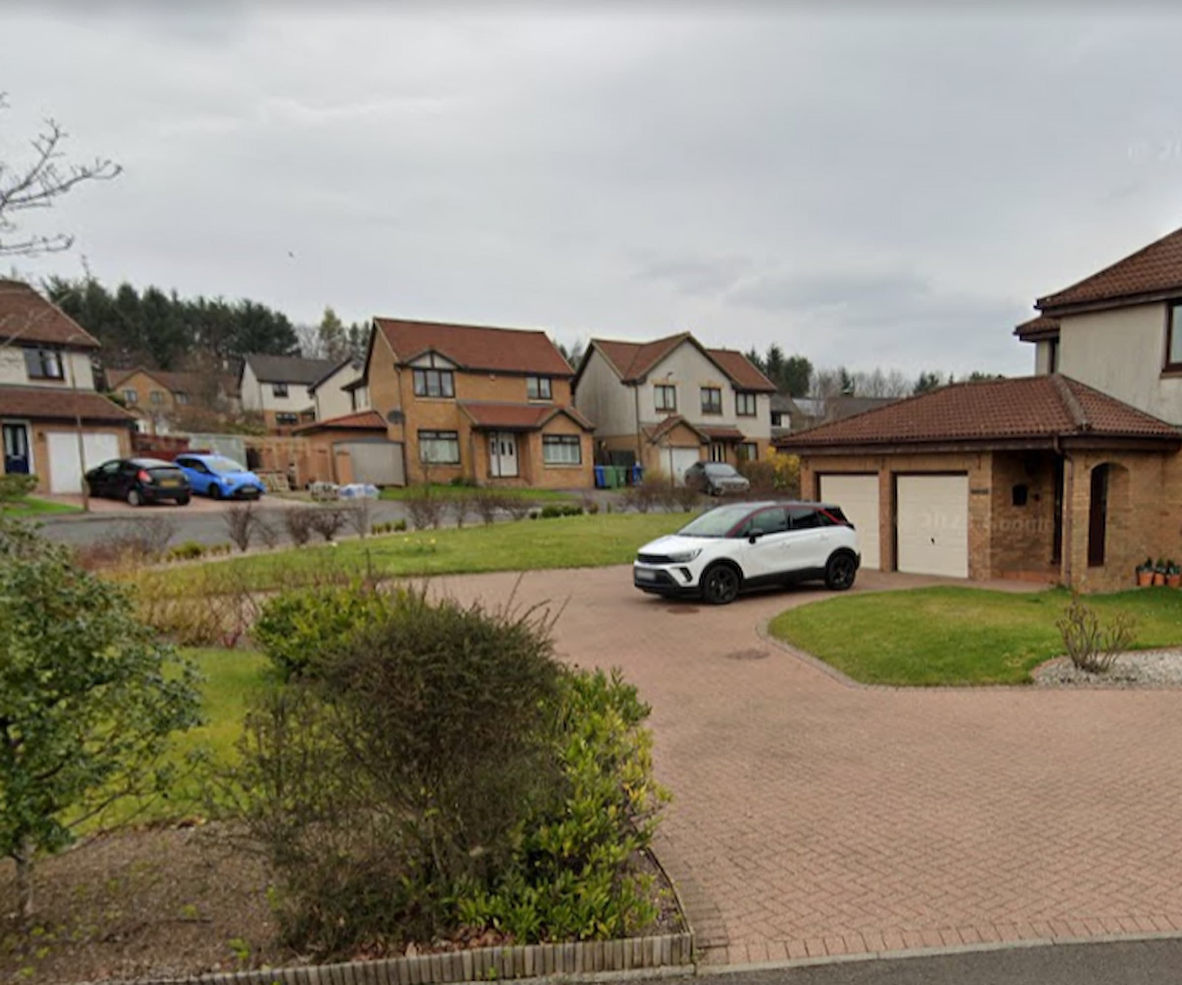 The front garden and brick driveway of a property on a roundabout