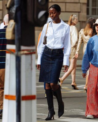 @sylviemus_ wearing a white button-down shirt and denim skirt with black boots.