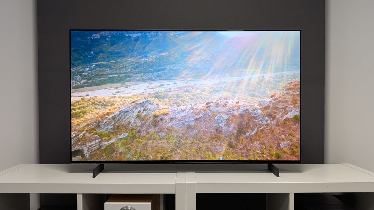The LG C5 42-inch OLED TV seen straight-on on a TV cabinet. On screen are rays of sunlight beaming down on a mountain road.