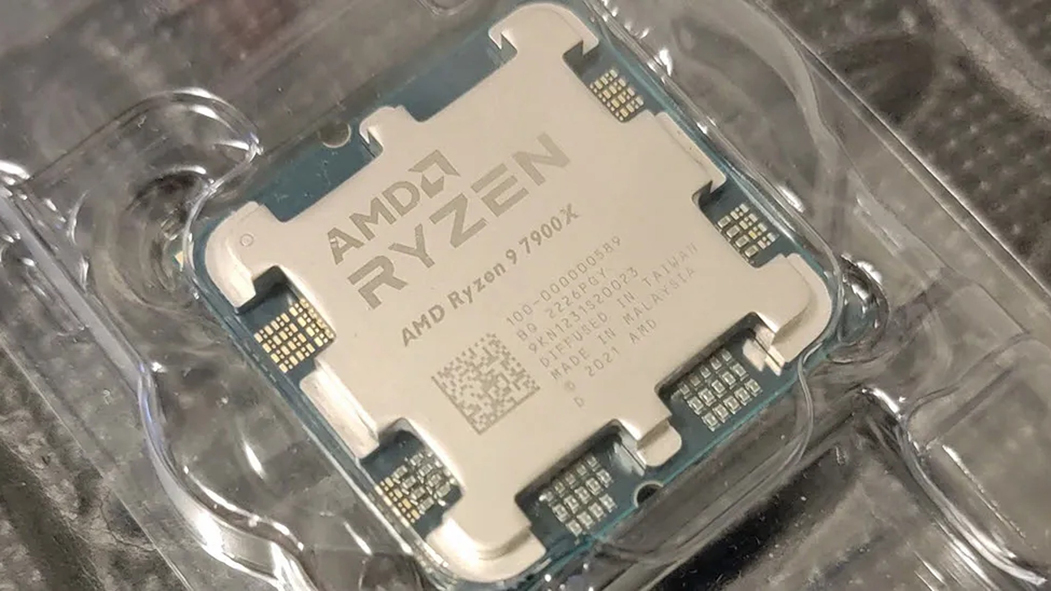 Close-up of an AMD Ryzen 7900X processor in clear packaging, showcasing its metallic surface and circuitry details. The tone is high-tech and sleek.