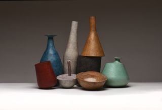 Contemporary crafted vessels in diferent shapes, colours and sizes photographed against a grey background