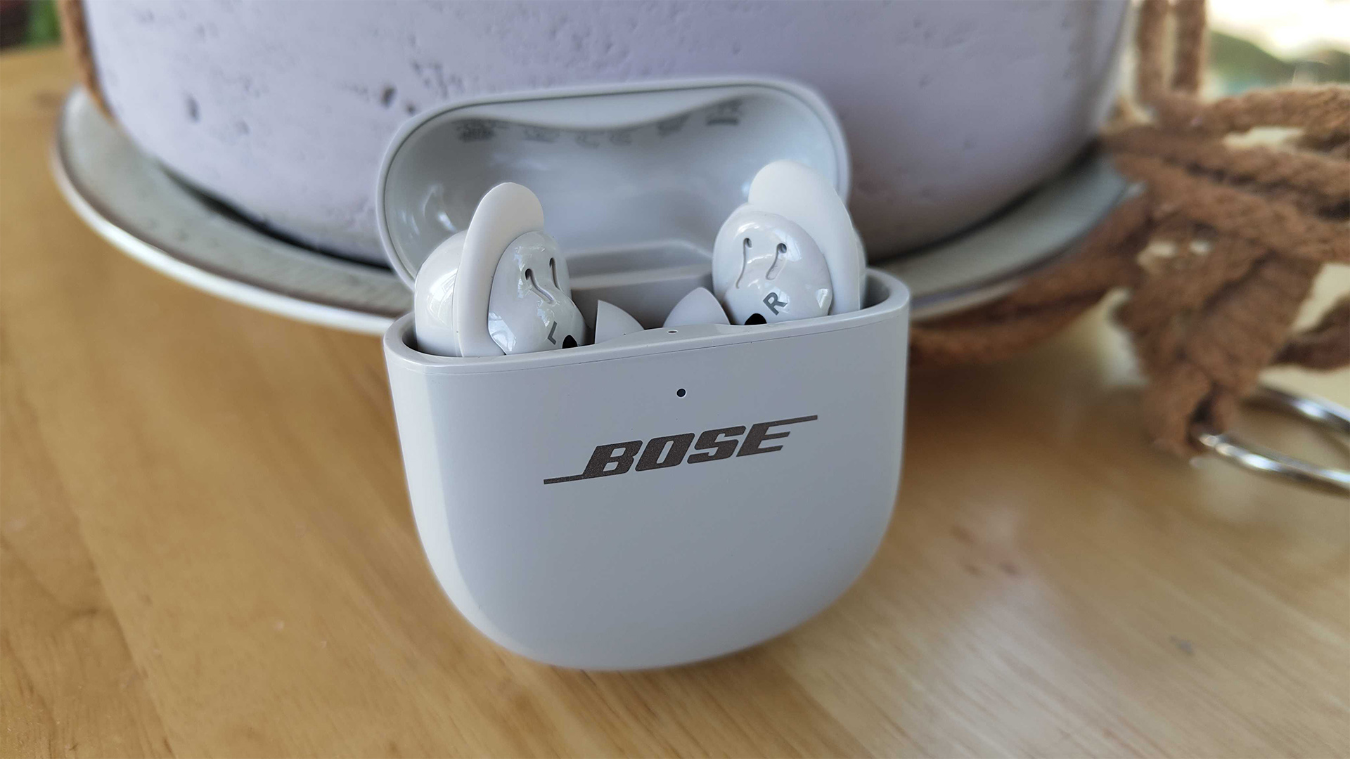Bose QuietComfort Ultra Earbuds (2nd Gen) wireless earbuds in case on wooden table leaning against plant pot