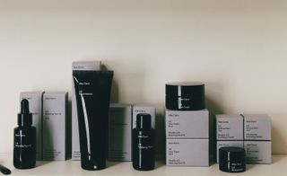 A display of Alex Carro's skincare capsule collection featuring the black containers with their packaging behind photographed against a grey wall
