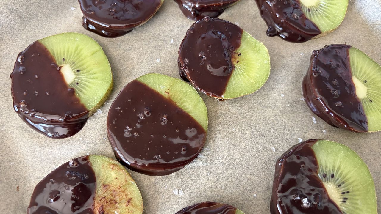 A close up of kiwi slices, dipped in dark chocolate and sprinkled with salt