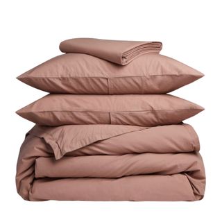 A terracotta bedding set, two pillows, and a sheet folded on top of each other