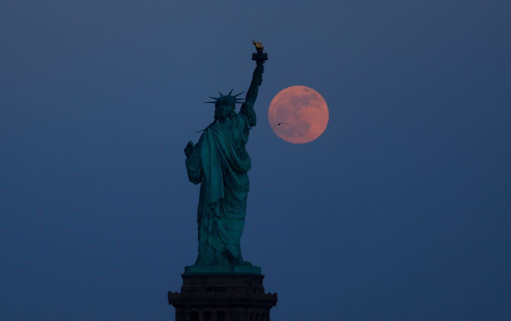 The full Flower Moon rises behind the Statue of Liberty at twilight in New York City on May 22, 2024, as seen from Jersey City, New Jersey