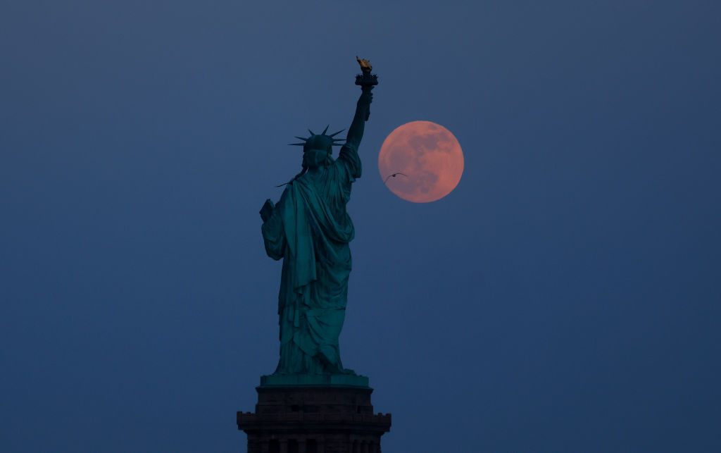 The full Flower Moon rises behind the Statue of Liberty at twilight in New York City on May 22, 2024, as seen from Jersey City, New Jersey