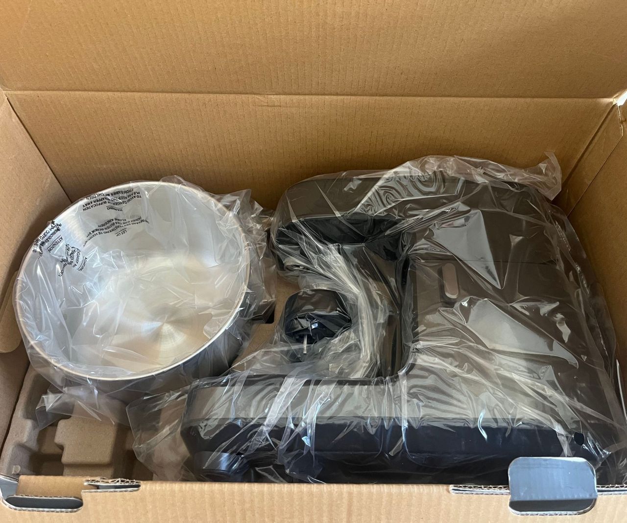 A black stand mixer and stainless steel bowl in bags in a cardboard box
