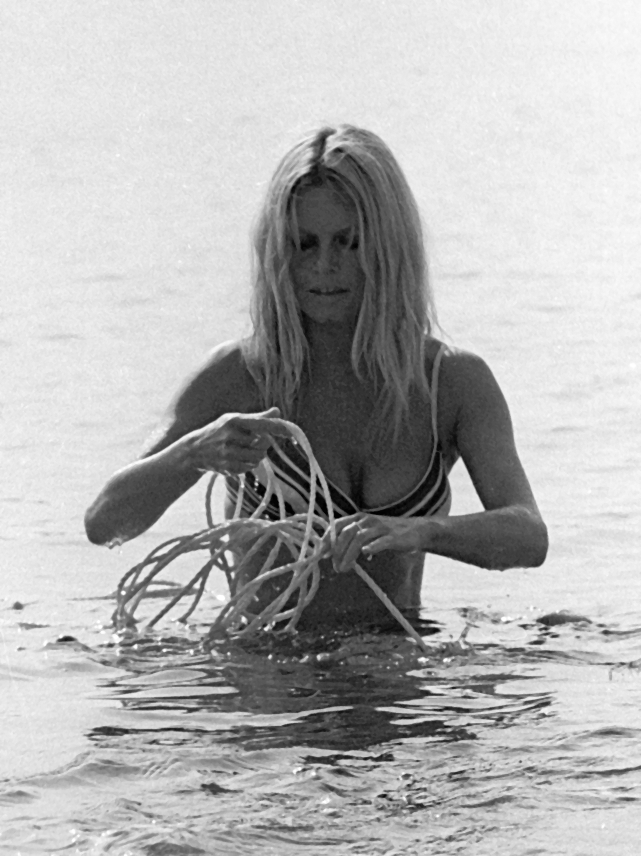 Brigitte Bardot untangling a knot of rope while standing in waist-deep water