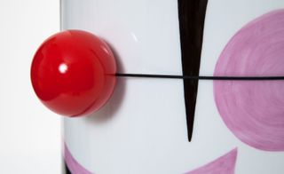 Red clown nose on a white charpin vase photographed against white background