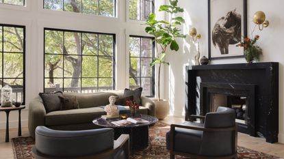 a light filled living room with large original windows, a black marble fireplace styled with sculptural furniture and a vintage rug