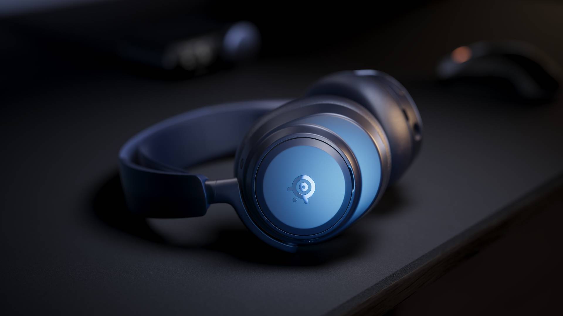 Image of the Midnight Blue Arctis Nova Pro Omni headset sitting on a black desk.