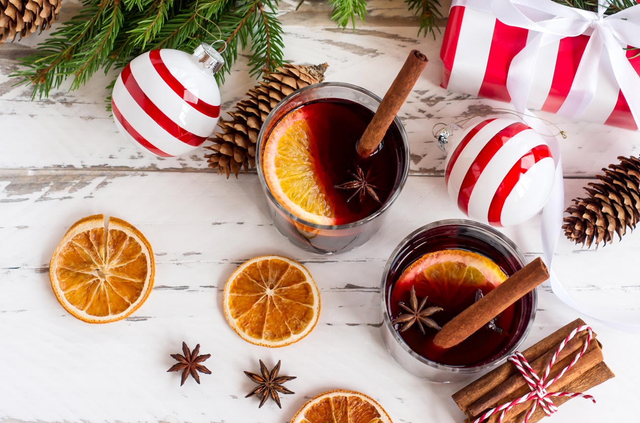 Two christmas cocktails on a white table with orange slices, star anise and baubles