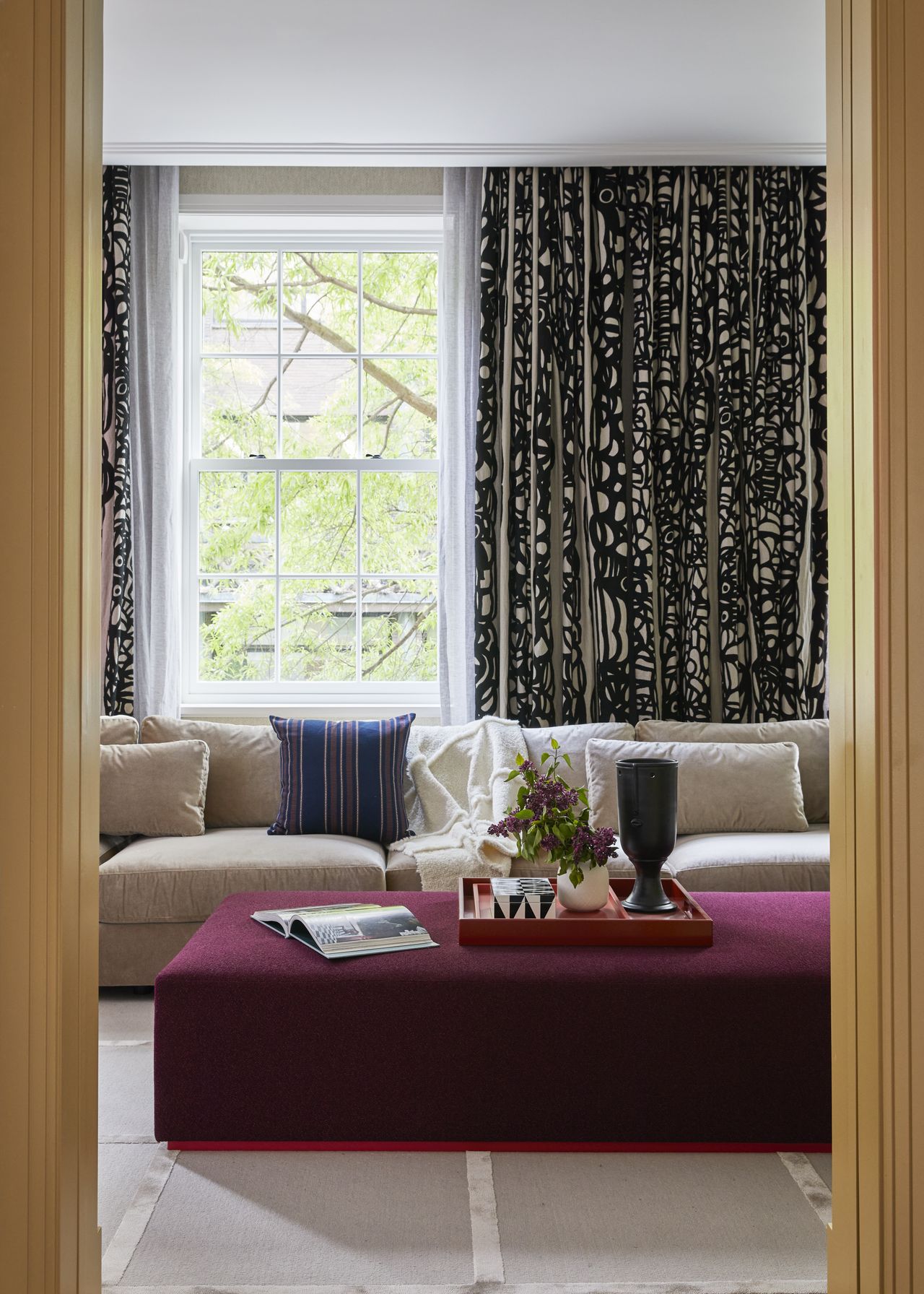 taupe living room with violet ottoman and yellow door trim, patterned curtains and cream couch