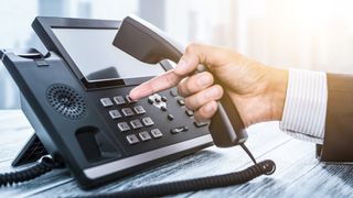 A hand reaching for a business phone.