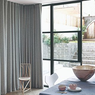 A dining room with glass doors opening onto a patio half covered with a grey curtain
