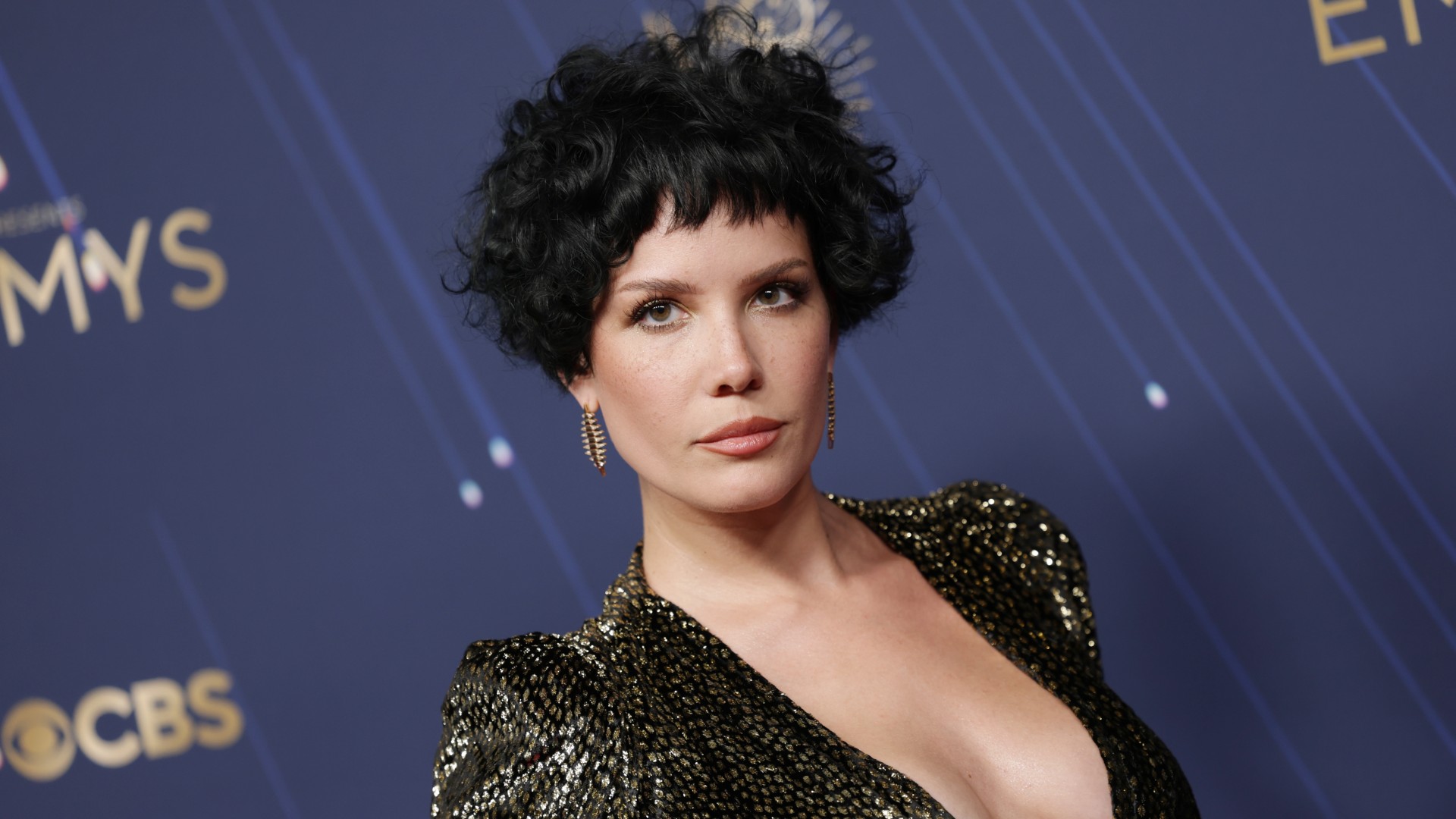 a woman with short, black hair poses in front of a blue backdrop