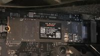 Close-up of a WD_Black SN7100 NVMe SSD installed on a motherboard. The SSD label displays its 1TB capacity and technical details.