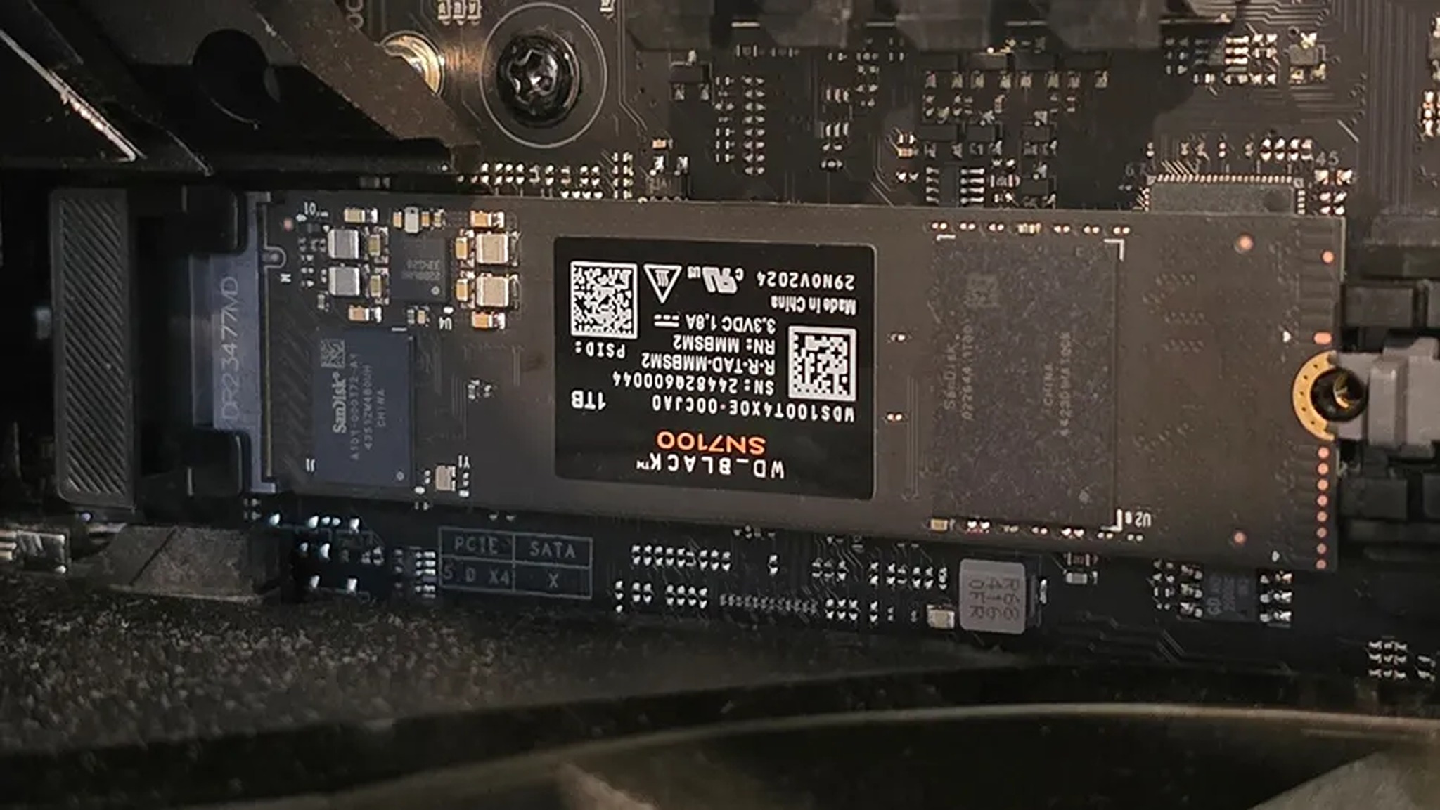 Close-up of a WD_Black SN7100 NVMe SSD installed on a motherboard. The SSD label displays its 1TB capacity and technical details.