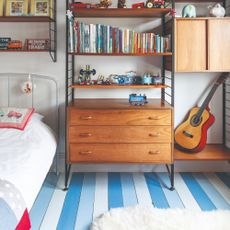 A child's bedroom with midcentury shelving and wooden floors painted in a striped pattern using different shades of blue