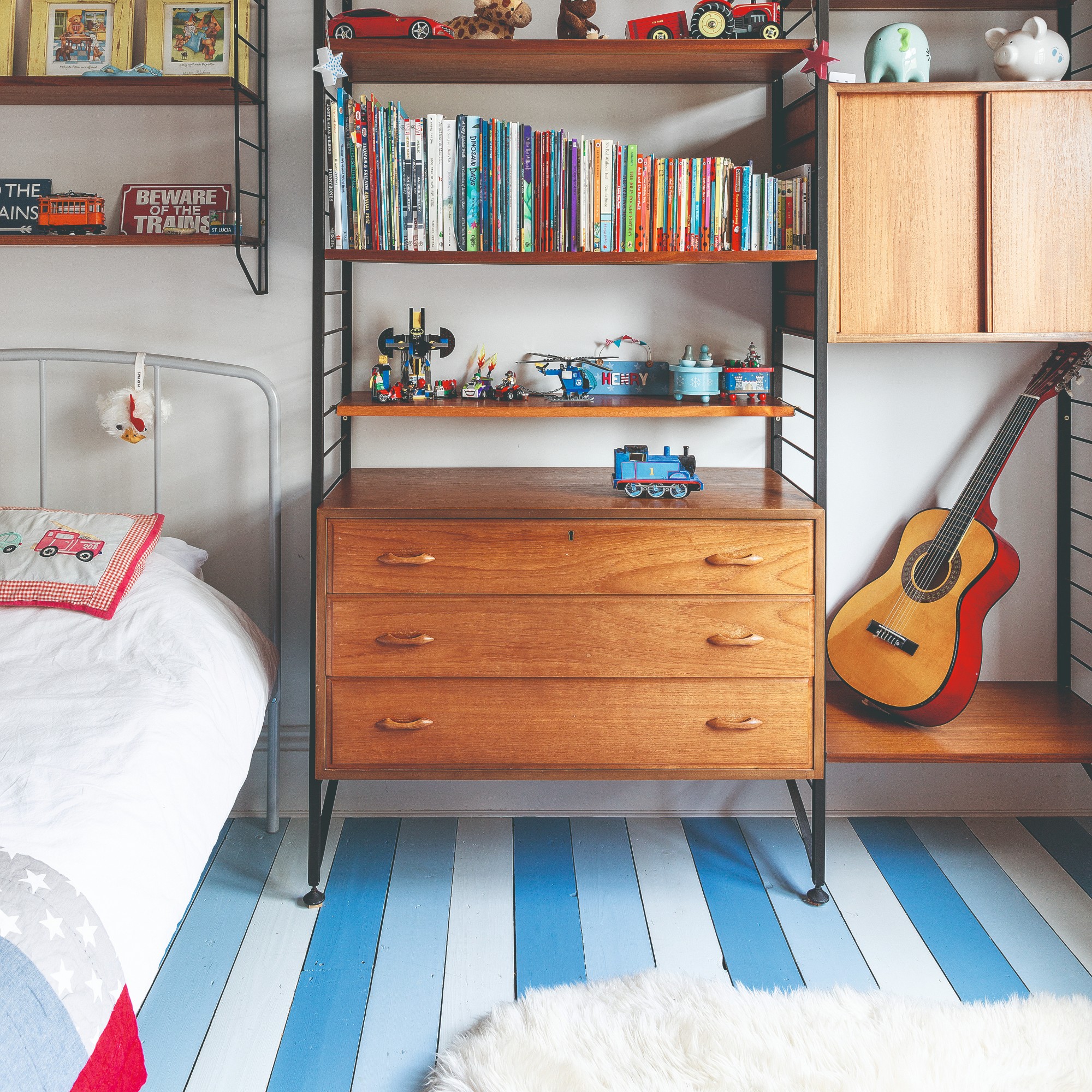 A child's bedroom with midcentury shelving and wooden floors painted in a striped pattern using different shades of blue