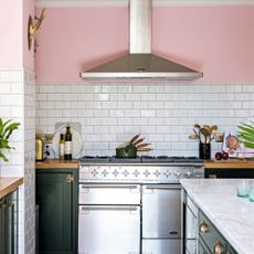 Open plan kitchen with pink walls, black Shaker style kitchen units, and rustic vintage furniture with stainless steel range cooker