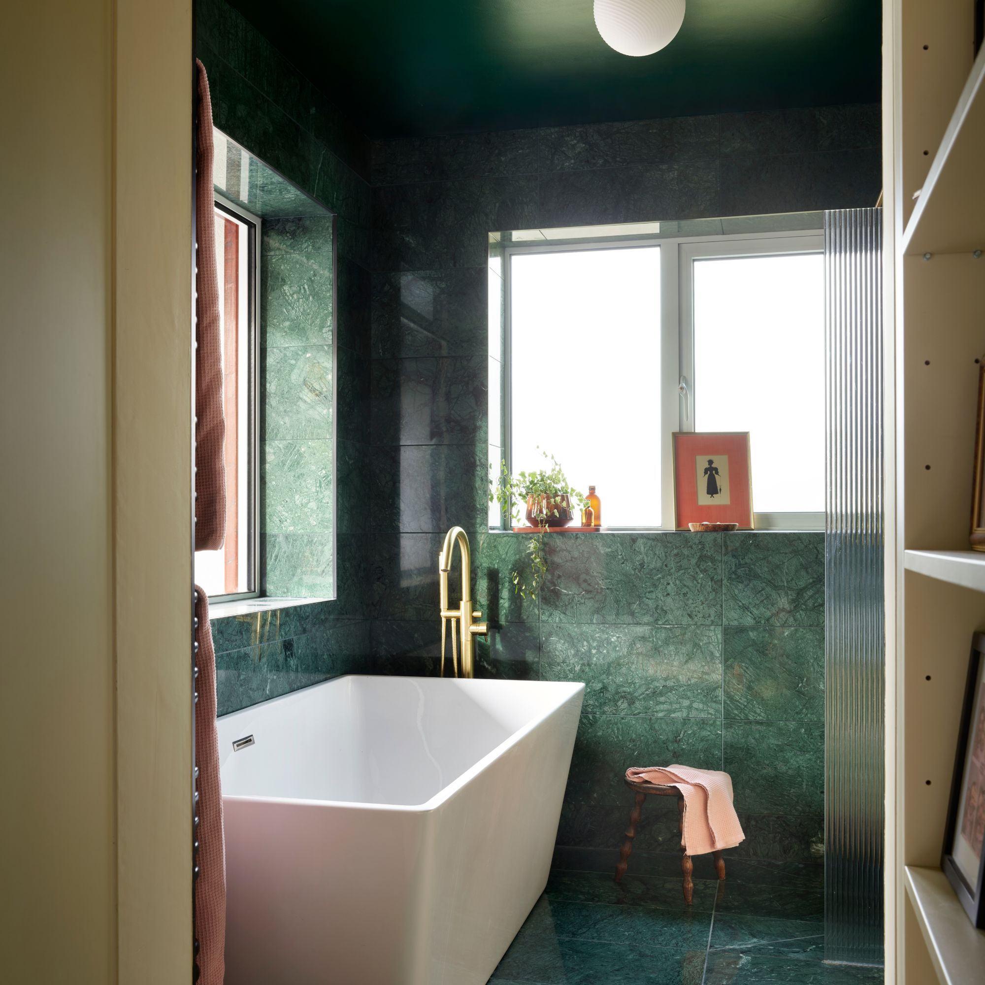 White rectangular bathtub with brass tap and green marble effect tiles on the wall and floor