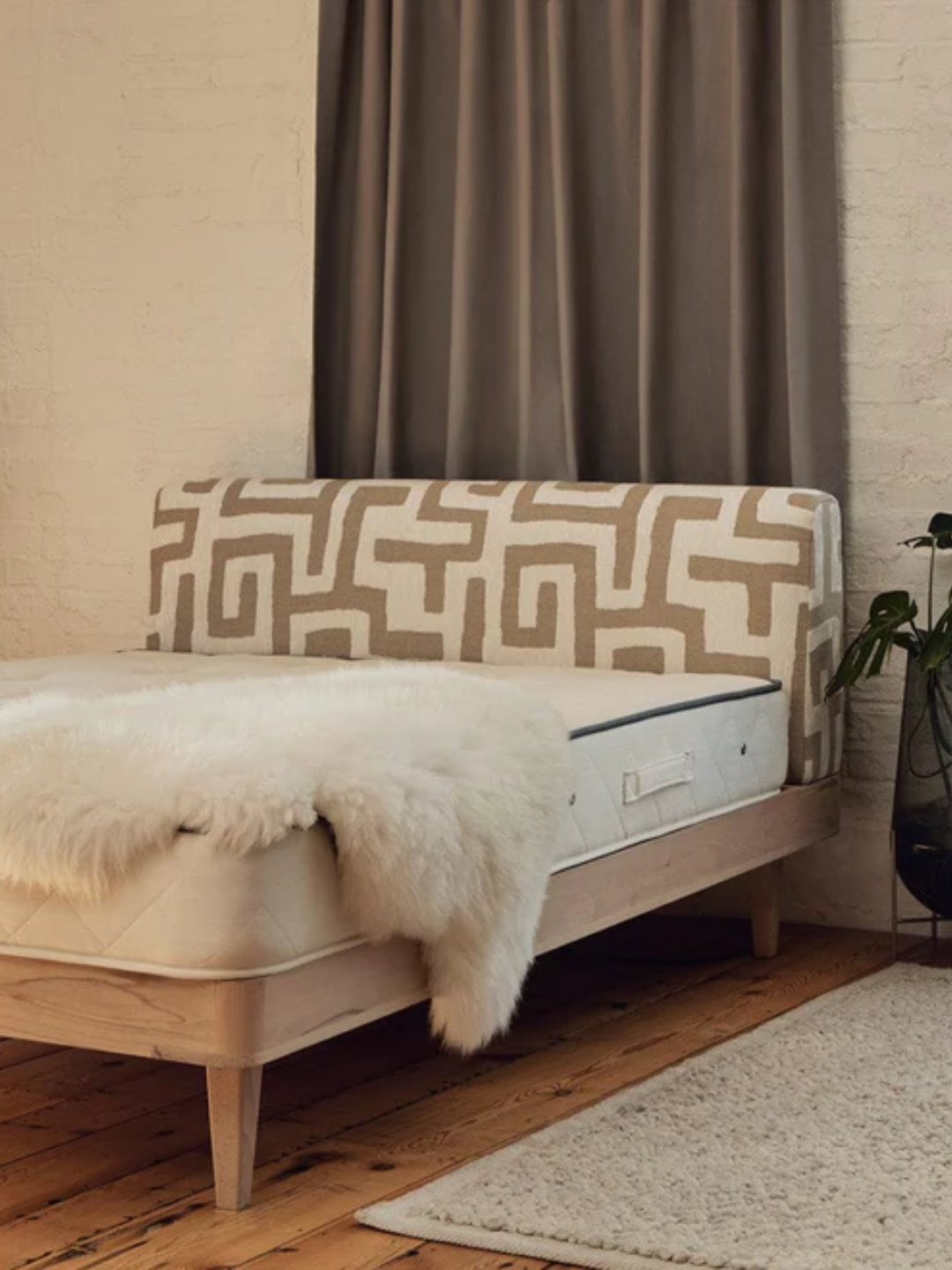A natural mattress on a bed with a patterned headboard with a white furry throw