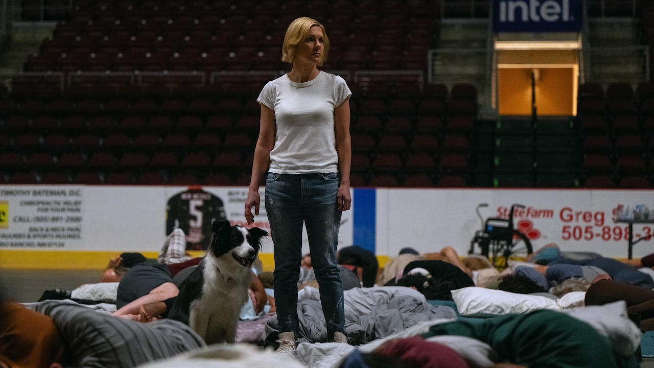 Carol standing in arena where Others are sleeping on floor in Pluribus Season 1