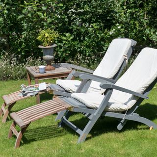 Painted wooden garden loungers with white cushions on a green grass lawn