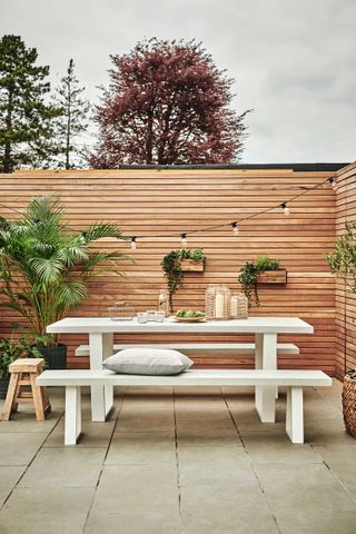 garden table ideas: white bench against panelled fence