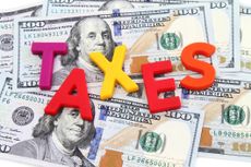 The word TAXES spelled out with colorful letters on scattered hundred dollar bills for paying the IRS