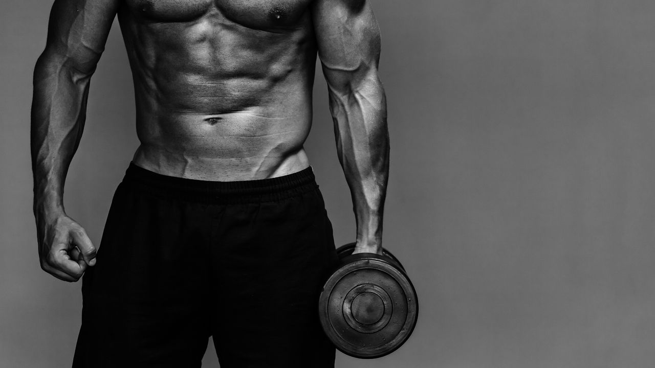 Close up of muscular bodybuilder guy doing exercises with weights over grey background. Black and white