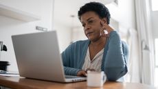 An older woman looks serious as she looks at her laptop at home.