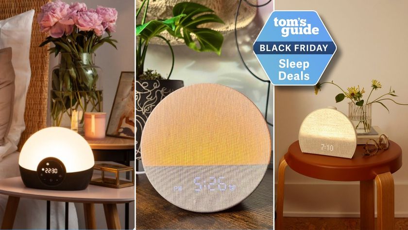 A college of three sunrise alarm clocks. Lumie Bodyclock Glow on bedside table (left). Dreamegg sunrise alarm clock with plant in background (middle). Hatch Restore 3 on circle wooden table with yellow flowers in pot (right), with Tom&#039;s Guide Black Friday sleep deals badge.