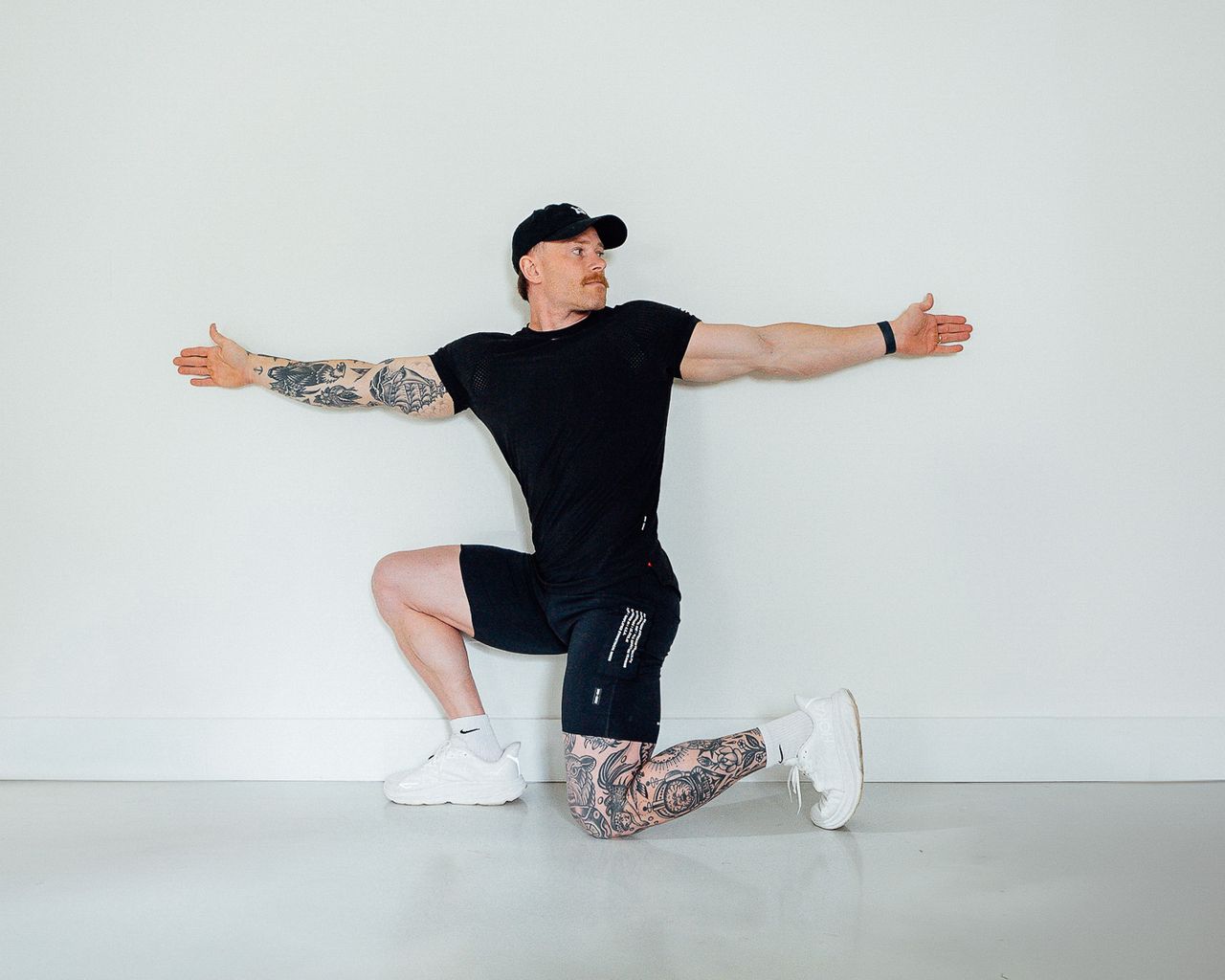 His left leg is bent at a 90-degree angle, with his knee and toes resting on the floor. His right leg is also at a 90-degree angle, but his right knee is up in line with his hip and the sole of his right foot rests on the floor. His torso is rotated towards his left hip and his arms are straight out to either side.