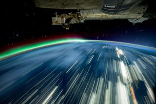 a long-exposure photo of earth with streaks of white and a green aurora on the horizon