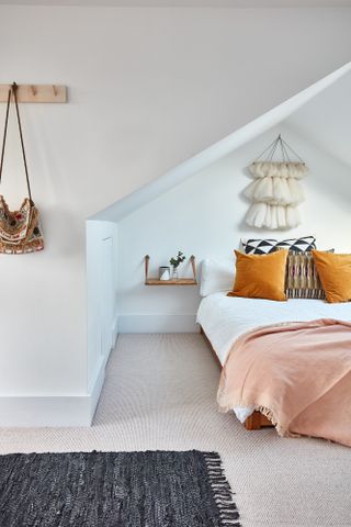 A loft bedroom with white wall paint decor, pink throw and wooden shelving