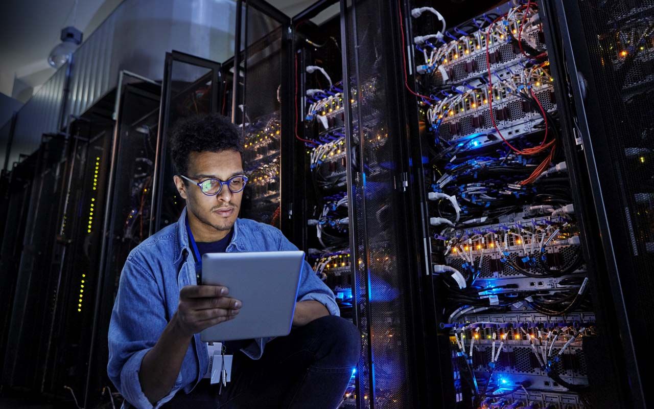 Focused male IT technician using digital tablet in dark server room